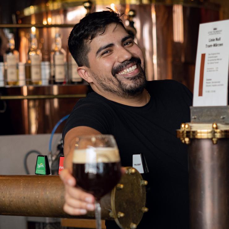Barmitarbeiter lacht in Kamera und stellt Bier auf Thresen